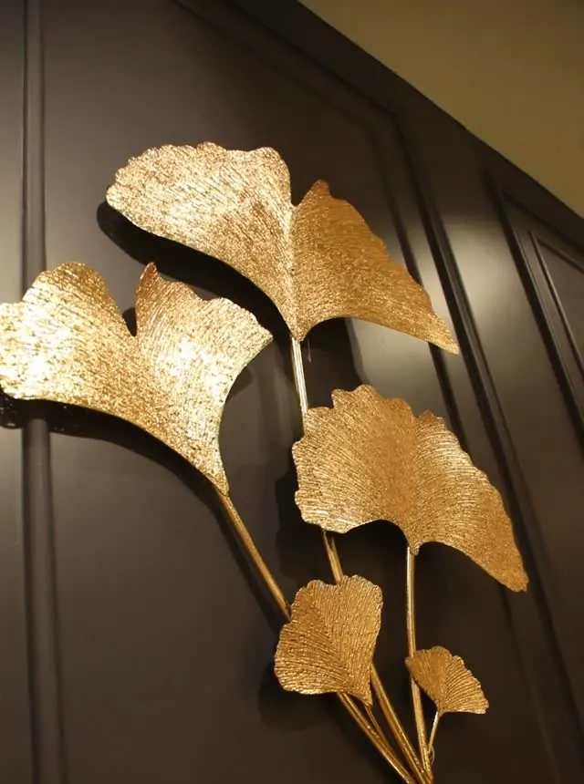 جدارية معدنية ذهبية على شكل أوراق الجنكة على جدار داكن